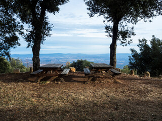 imagen de dos mesas de madera de picnic en la montaña, entre los árboles, con vistas al valle 