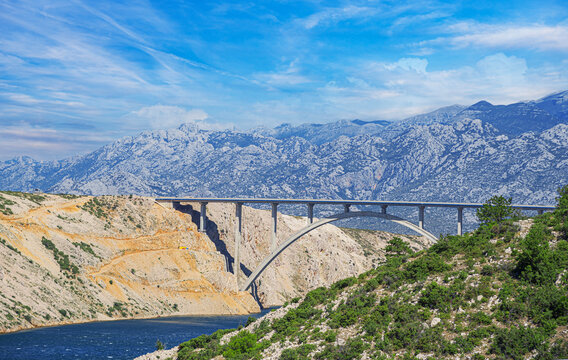 Concrete arch bridge with a road against the backdrop of mountains.