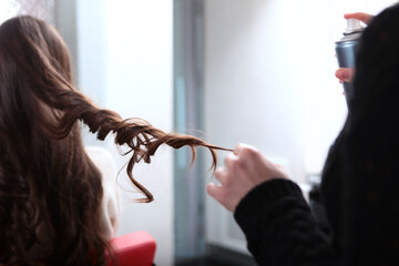 A professional hairdresser applies hairspray to a young woman's hair. Fixation of curls. Hair...