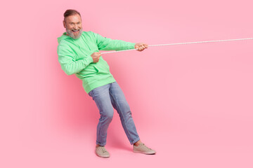 Full size photo of cool pensioner man pulling string strength wear trendy green clothes isolated on pink color background