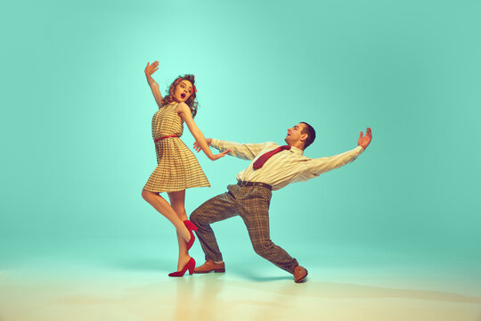 Two dancers, man and woman dressed retro outfits in mid-twirl, embodying 50s swing dance enthusiasm against gradient mint background. Concept of music, energy, art, happiness, mood, action