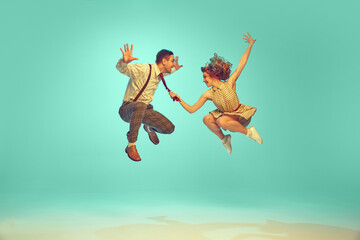 Portrait of modern jazz-dancers in mid-air against gradient mint background. Joyful dance partners performing dance. Vintage fashion. Concept of music, energy, happiness, mood, action