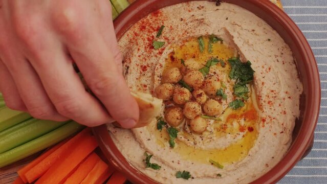Hummus among fresh vegetables on table top view. Hummus garnished with chickpeas, olive oil, spices and greens. Hummus or fava, a hearty snack of legumes. Kosher healthy vegan food. Lean