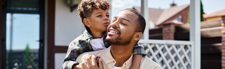 cute african american boy hugging excited father in braces on backyard of house, banner