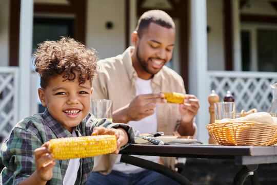 cheerful african american kid having family bbq with father on backyard of house, orange juice
