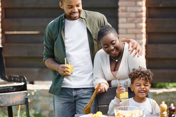 african american parents looking at joyful son holding glass of orange juice on backyard during bbq