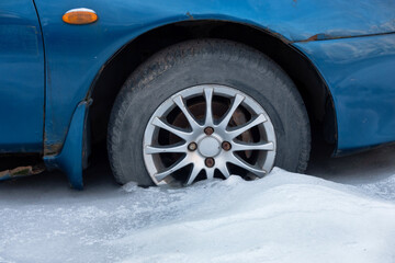 The front wheel of an old blue car frozen in ice. There are dents and rust on the body. Close-up. Background.
