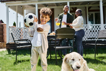 family time, joyful african american kid holding football near parents and dog on backyard of house
