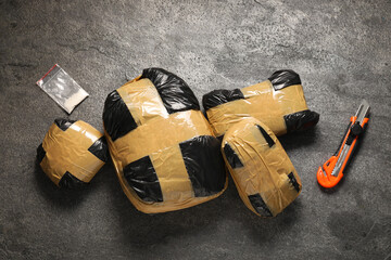 Packages with narcotics and stationery knife on grey textured table, flat lay
