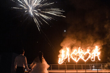 Fire show. The newlyweds hold hands against the background of fiery hearts and fireworks. Wedding, show program.