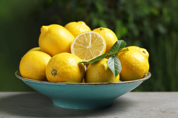 Fresh lemons and green leaves on grey table outdoors