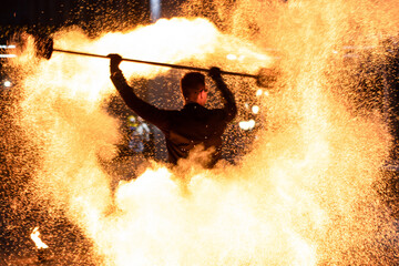A young man and a girl dancing with fire. Fire show, artist. Show program, in the evening on the street. Fire fans. Slow motion.