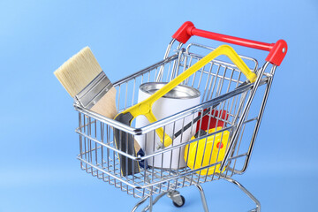 Small shopping cart with paint and renovation equipment on light blue background