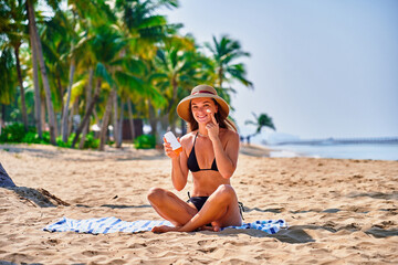 Satisfied young joyful happy smiling woman using facial spf sunscreen while sunbathing and relaxing in the sun. Sunburn protection and healthy skin