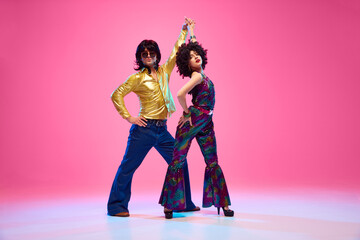Groovy dance couple in bright attire performing disco moves in motion against gradient pink studio...