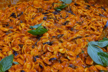 Orecchiette alla siciliana con sugo di pomodoro, melanzane fritte, ricotta salata e basilico fresco pronte per essere impiattate in un ristorante da cerimonia