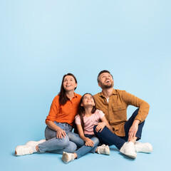Joyful family of three looking up sitting on blue background