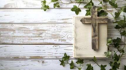 Cross laying on top of opened white Christian bible with green vine border on white wood background
