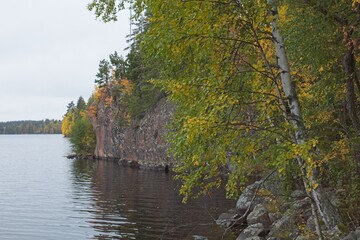 View of lake shore with trees and bluff in cloudy autumn weather.