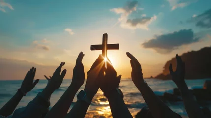 Gardinen In the background of a sunset, a group of hands is praying and holding a christian cross. Silhouette shows hands holding the cross as they worship God. © Zaleman