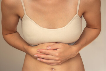 A young woman in beige underwear holds her stomach with both hands, experiences severe acute...