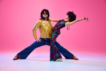 Lost in Rhythm. Young couple, man and woman in bright retro costumes in dance pose against gradient pink studio background. Concept of American culture, 70s, 80s fashion, music, comparisons of eras.