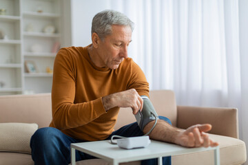 Handsome grey-haired senior man checking blood pressure at home