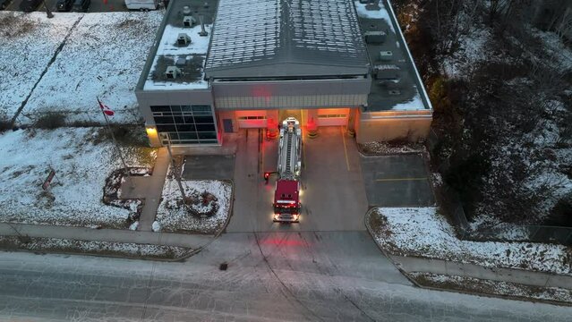 Cinematic drone shot American fire truck leaving fire station during fire or disaster relief and first aid, Dartmouth, Canada. Aerial view of fire engine with ladder and siren on near station building