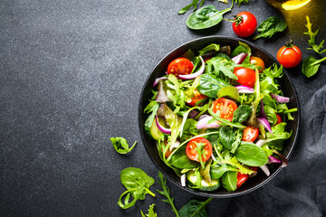 Salad in black bowl at dark background.