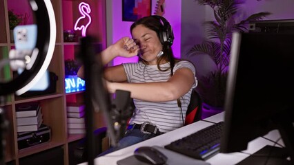 A young woman enjoys gaming in a vibrant room with neon lights, headphones, and modern computer setup.