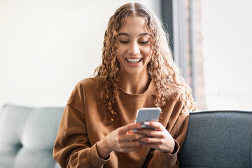 Happy zoomer girl smiling while texting on her phone indoors