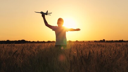 Cheerful boy teen running with plane toy on autumn wheat field at cinematic sunset sunrise back...