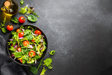 Salad in black bowl at dark background.