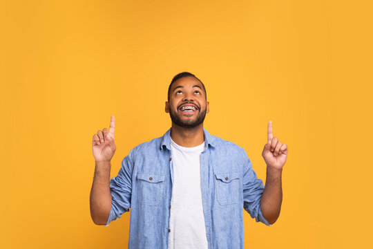 Happy young black man pointing up at copy space with two hands