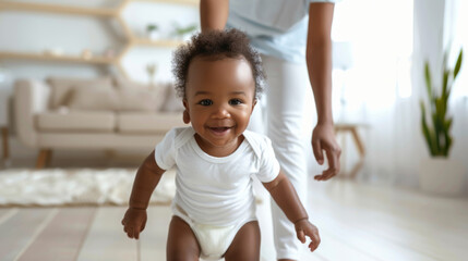 joyful baby is taking steps towards the camera while holding an adult's hand, likely taking some of their first steps in a cozy home environment. - obrazy, fototapety, plakaty