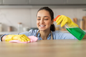 Happy woman with spray bottle cleaning countertop