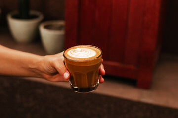 Female hand holding glass cup with coffee. Delicious cappuccino with almond milk. Woman drinking coffee for breakfast