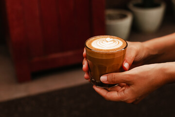 Female hands holding glass with delicious latte. Coffee with almond milk. Delicious, high-quality...