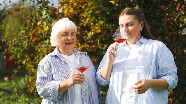 Two women of different ages are celebrating something at backyard at garden. Pretty middle aged woman and her adult daughter drinking wine, summer day. 