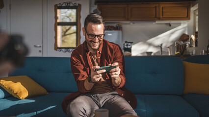 Obraz premium caucasian man sit at home play video games on smartphone mobile phone