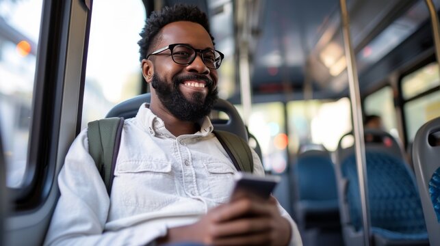 African American man smiling while using smartphone on city bus. Cheerful passenger enjoying his journey on public transport. Casual urban travel concept. Everyday commute scene