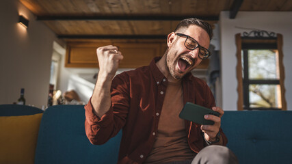 caucasian man sit at home play video games on smartphone mobile phone