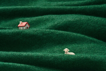 Miniature Homestead on Woolen Pasture. Tiny sheep and house figurines on a green wool fabric depicting a pastoral scene.