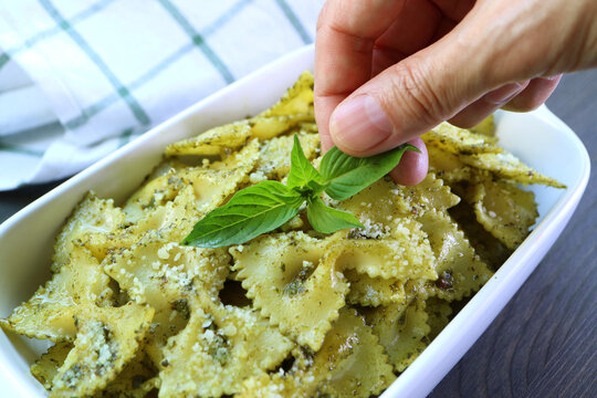 People Garnishing Freshly Cooked Pesto Farfalle Pasta Dish with Fresh Basil Leaves