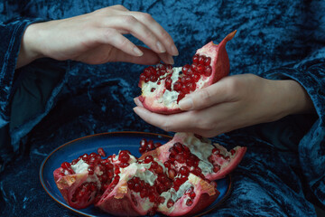 Person delicately separating pomegranate seeds over a blue velvet backdrop. Close-up shot with rich...