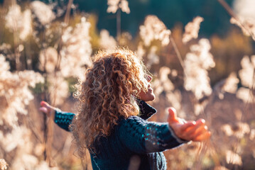 Back side view of woman enjoying sunset in golden field of grass opening outstretching arms alone....