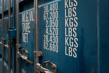 Shallow focus of a generic, standing shipping container showing weight measurements on one of the...