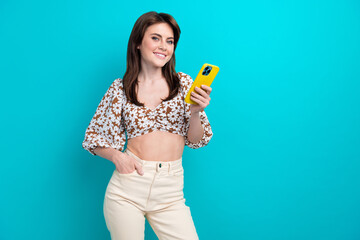 Portrait of happy young woman in trendy glamour apparel buying clothes online using smartphone isolated on aquamarine color background