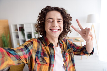 Photo of cool cheerful guy dressed checkered shirt tacking selfie showing v-sign indoors house home room