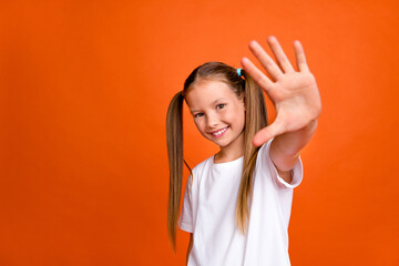 Photo of cheerful lovely girl toothy smile arm palm waving hi empty space isolated on orange color...